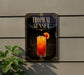 A sign for a tropical sunset cocktail is displayed on a wall, with a plant visible to the left.