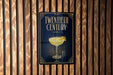 A sign for a "Twentieth Century" cocktail, featuring an illustration of a cocktail glass with a lemon twist on a dark background.