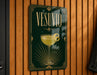 A framed poster with the word "VESUVO" prominently displayed, featuring an illustration of a cocktail glass with a lemon twist.
