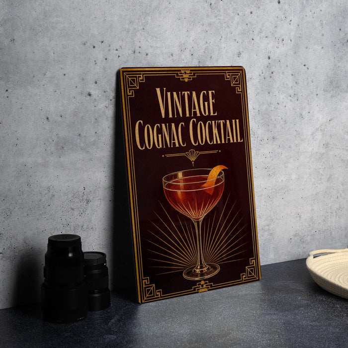 A vintage cognac cocktail sign is displayed on a gray countertop, accompanied by a stack of black camera lenses and a white dish.