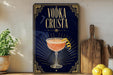 a decorative sign with a cocktail illustration, placed on a wooden surface next to a wooden cutting board and some lemons.