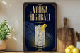 A framed advertisement for vodka highball, featuring a glass of highball cocktail with a lemon slice, placed on a wooden shelf next to a wooden cutting board and a potted plant.