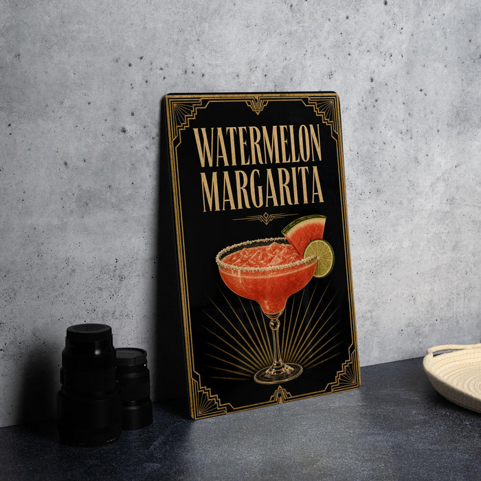 A framed poster of a watermelon margarita is displayed on a gray wall, with a stack of black cups and a white dish visible to the side.