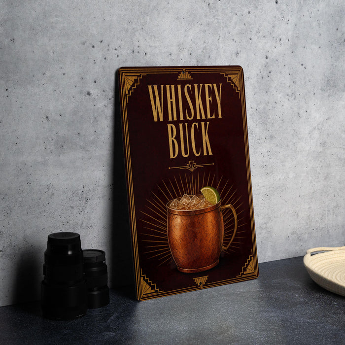 A metallic sign with the text "Whiskey Buck" and an illustration of a copper mug with a lime slice, placed on a gray countertop next to some black containers.