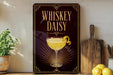 A decorative sign for whiskey daisy cocktail, featuring a glass of the cocktail and a lemon peel, is displayed on a shelf next to a wooden cutting board and a potted plant.
