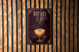 A sign for a whiskey flip cocktail is displayed on a wooden wall.