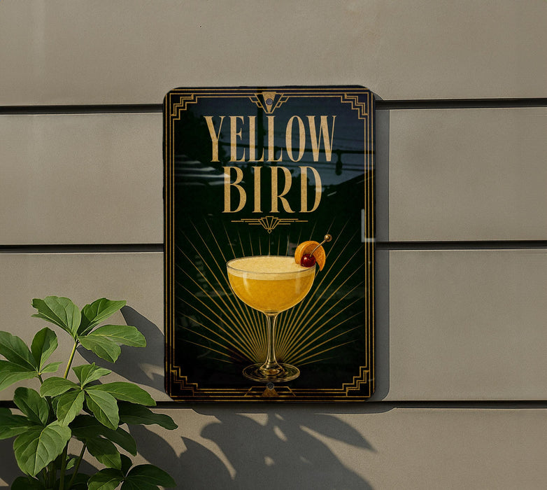 A sign for a cocktail called "Yellow Bird" is displayed on a wall, featuring an illustration of a cocktail glass with a garnish.