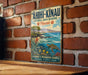 A vintage metal sign with a tropical beach scene and a sea turtle, mounted on a brick wall.