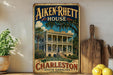 a vintage-style sign for the Aiken-Rhetts House in Charleston, South Carolina, with a tropical house illustration and the text "Step into history" and " Charleston South Carolina".