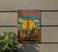 A vintage-style metal sign with the text "AKSUM Ethiopia" and an illustration of the ancient city of Akosma, featuring tall obelisks and other landmarks.
