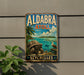 A vintage metal sign with a tropical beach scene, featuring a large turtle, palm trees, and a bird, mounted on a wall.