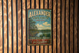 A vintage-style metal sign for Alexander State Forest in Louisiana, featuring a scenic landscape with a river and pine trees.