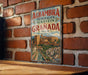 A vintage-style metal sign with the text "Alhambra Generalife Albayzin Granada Spain" is displayed on a brick wall.