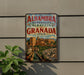 A vintage-style metal sign with the text "Alhambra Generalife Albayzin Granada Spain" displayed on a wall, featuring an illustration of a cityscape with a castle and a fountain.