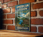 A vintage-style metal sign for the American Legion State Forest in Connecticut, featuring a scenic landscape with pine trees and a lake.
