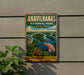 a vintage-style metal sign with a painting of a bird and a dolphin, set against a backdrop of a river and lush vegetation, with the text "ANAVILHANAS NATIONAL PARK BRAZIL" prominently displayed.