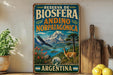 A vintage-style metal sign with the text "RESERVA DE BIOSFERA ANDINO NORPATAGONICA ARGENTINA" and an illustration of a mountain, a bird, and a deer. The sign is displayed on a shelf next to a wooden cutting board and a potted plant.