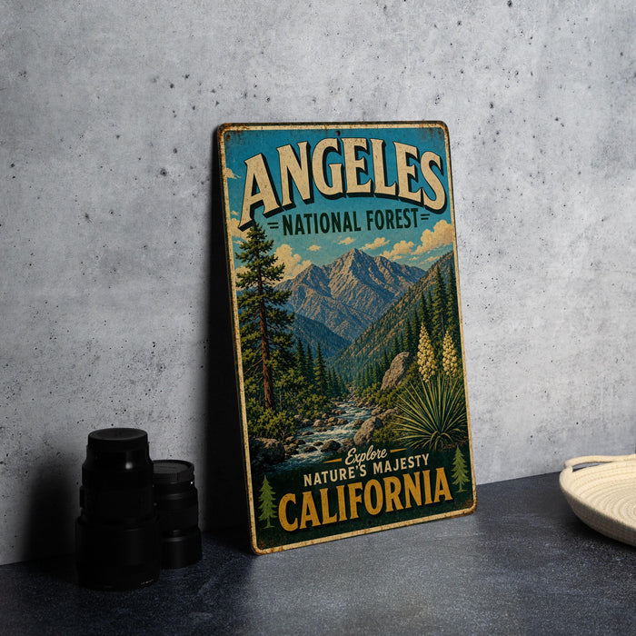A vintage metal sign for the Angeles National Forest in California, featuring a scenic mountain landscape with pine trees and a river.