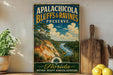 A vintage-style sign for the Apalachicola Bluffs & Ravines Preserve in Florida, featuring a scenic landscape with a river and palm trees.