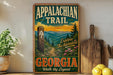 A vintage trail sign for the Appalachian Trail in Georgia, featuring a scenic mountain landscape with pine trees and a winding path.