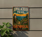 A vintage metal sign on a wall, featuring the text "Appalachian Trail Georgia" and an illustration of a mountain landscape with pine trees and a trail.