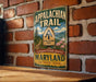 A vintage metal sign for the Appalachian Trail hangs on a brick wall, featuring a scenic illustration of the trail and the words "Appalachian Trail" and "A Footpath Through America".
