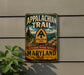 A vintage metal sign for the Appalachian Trail in Maryland, featuring a scenic mountain landscape and the trail's name.