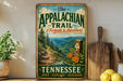 A vintage-style metal sign for "The Appalachian Trail" in Tennessee, featuring a scenic mountain landscape with a trail marker and the text "A Footpath to Adventure" and " Tennessee Hike - Explore - Discover".
