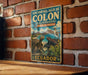 A vintage-style metal sign with the text "Archipielago de COLON (GalaPago) RESERVA DE BIOSFERA" and "ECUADOR" is displayed on a brick wall.