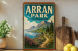 A vintage-style sign for Arran Park, United Kingdom, featuring a scenic mountain landscape with a winding path and a body of water.