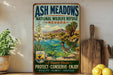 A vintage-style sign for the Ash Meadows National Wildlife Refuge in Nevada, featuring a desert landscape with a bird and a river.