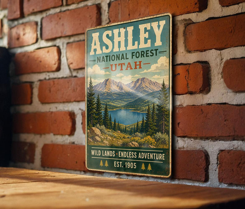 A vintage-style metal sign for the Ashley National Forest in Utah, featuring a scenic mountain landscape with pine trees and a lake.