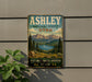 A vintage-style metal sign for the Ashley National Forest in Utah, featuring a scenic landscape with mountains, pine trees, and a lake.