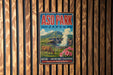 A vintage-style metal sign for Asop Park in Japan, featuring a cow grazing in a mountainous landscape with a steam vent in the background.