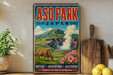 A vintage-style poster advertising ASO PARK, Japan, featuring a cow grazing in a mountainous landscape with a hot spring in the background.