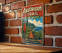 A vintage-style metal sign with a tropical island landscape and trail, mounted on a brick wall.