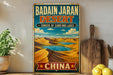 A vintage-style metal sign advertising the Badain Jaran Desert in China, featuring a desert landscape with sand dunes and a lake.