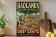A vintage-style metal sign advertising Badlands Cultural Landscape South Dakota, featuring a cowboy on horseback and a mountainous landscape.