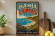 A vintage-style poster advertising Bahía Lomas, Chile, featuring a scenic coastal landscape with mountains, a beach, and a blue sky with clouds.