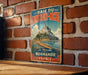 A vintage metal sign with the text "BAIE DU MONT SAINT-MICHEL" and "La Merveille" is displayed on a brick wall.