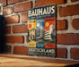 The image is a vintage-style poster advertising Bauhaus architecture, featuring a brick wall backdrop and a wooden table.