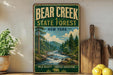 A vintage-style sign for Bear Creek State Forest in New York, featuring a scenic illustration of a forest with a river and mountains in the background.