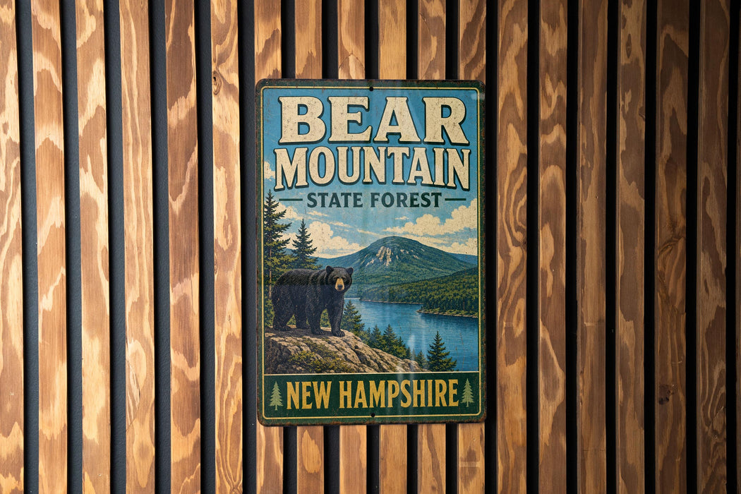 A vintage metal sign for Bear Mountain State Forest in New Hampshire, featuring a bear standing on a rocky outcropping overlooking a lake surrounded by pine trees.