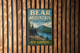 A vintage metal sign for Bear Mountain State Forest in New Hampshire, featuring a bear standing on a rocky outcropping overlooking a lake surrounded by pine trees.