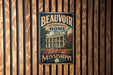 A vintage-style metal sign with the text "BEAUVOUIR JEFFERSON DAVIS HOME" and "PRESERVING HISTORY MONSTERING A LEGACY MISSISSIPPI" is displayed on a wooden wall.