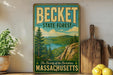 A vintage-style metal sign for the Becket State Forest in Massachusetts, featuring a scenic landscape with pine trees, a lake, and mountains.