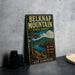 A vintage metal sign for Belknap Mountain State Forest in New Hampshire, featuring a scenic landscape with a lake, mountains, and pine trees.