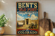 A vintage-style sign for Bent's Old Fort, a National Historic Site in Colorado, featuring a wagon and a cannon in the foreground.
