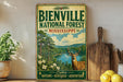 a vintage-style metal sign for Bienville National Forest in Mississippi, with a deer illustration and the text "Explore Nature - Heritage - Adventure" prominently displayed.