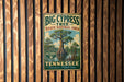 A vintage-style metal sign for Big Cypress Tree, located in Tennessee, is displayed on a wooden wall.